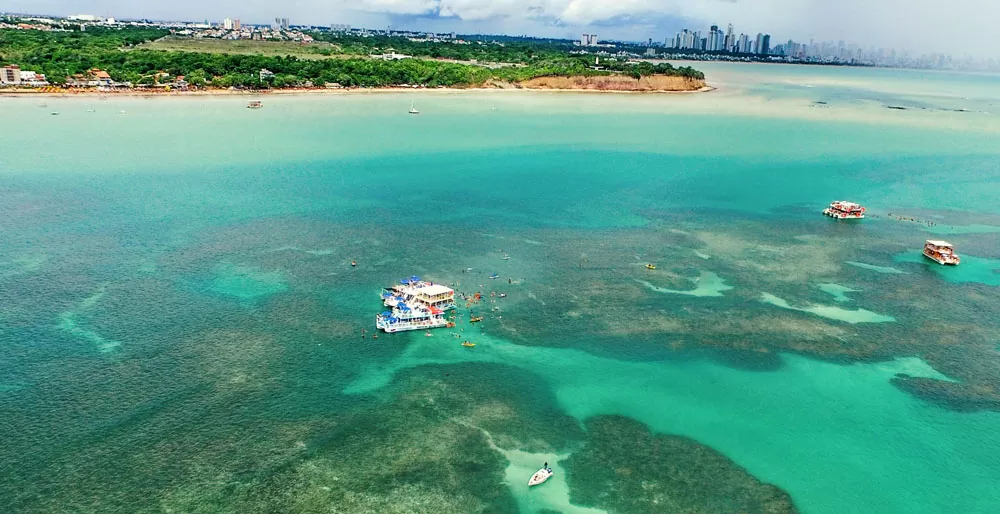 viajantes nadam perto de catamarãs em Piscinas Naturais do Seixas, uma das atrações entre muito o que fazer em João Pessoa