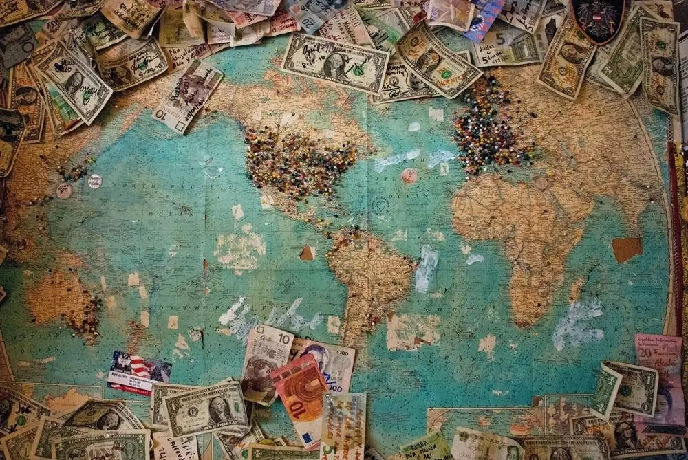 Notas dinheiro em cima de mapa mundil, que devem ser guardadas por quem quer juntar dinheiro para viajar
