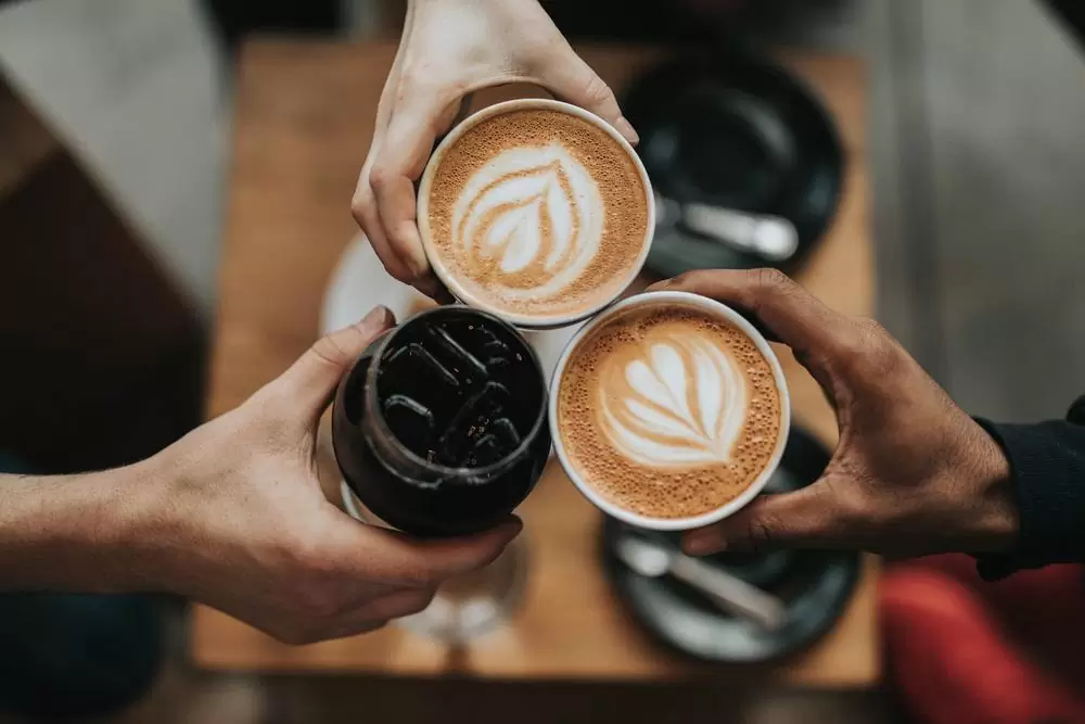 Pessoas brindam com café de cafeteria, que deve ser evitado por quem quer juntar dinheiro para viajar