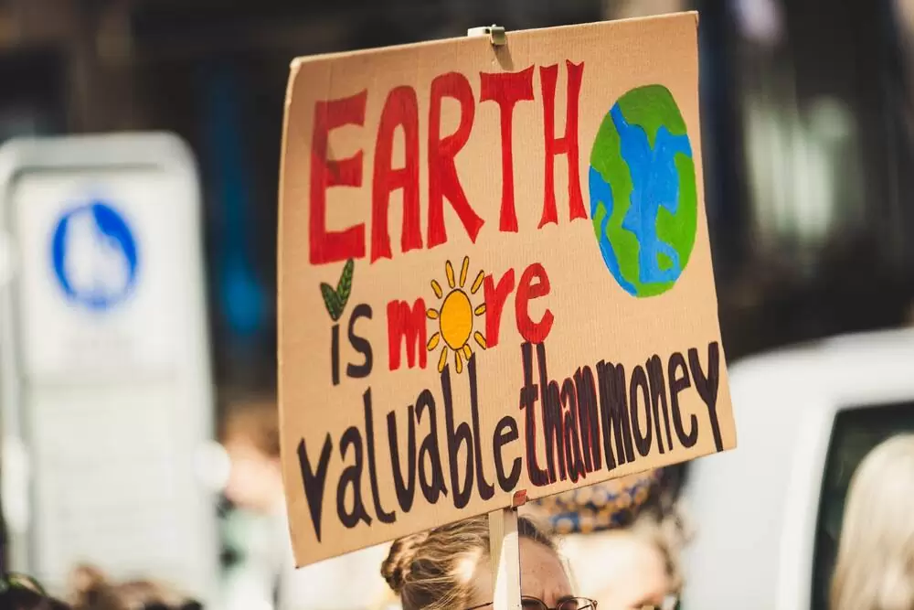 Mulher segura cartaz onde há escrito: earth is more valuable than money (a terra é mais valiosa do que dinheiro)