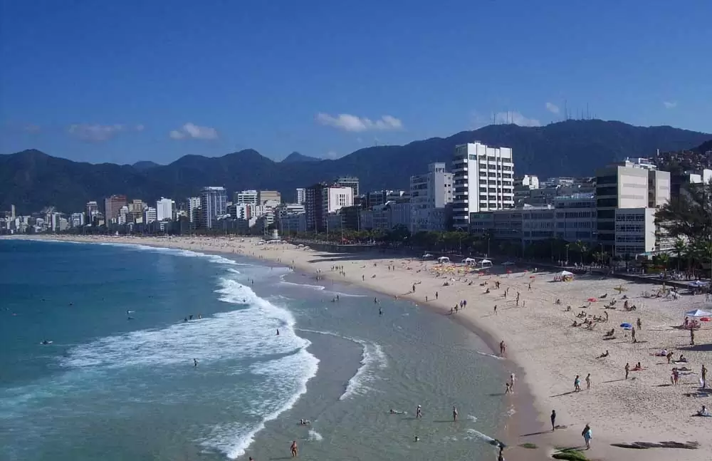 Pessoas na areia e no mar, em praia do Rio de Janeiro, durante o dia, um dos principais passeios do rj