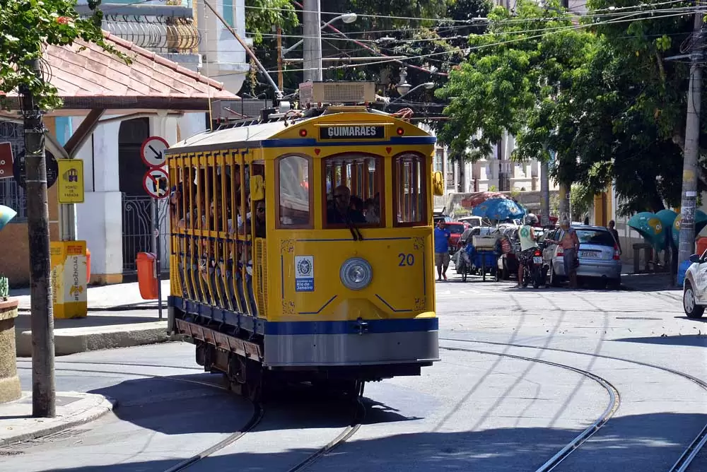 pessoas em bonde amarelo e azul em uma rua de Santa Teresa, bairro onde há muitos atrativos para quem busca o que fazer no Rio e Janeiro