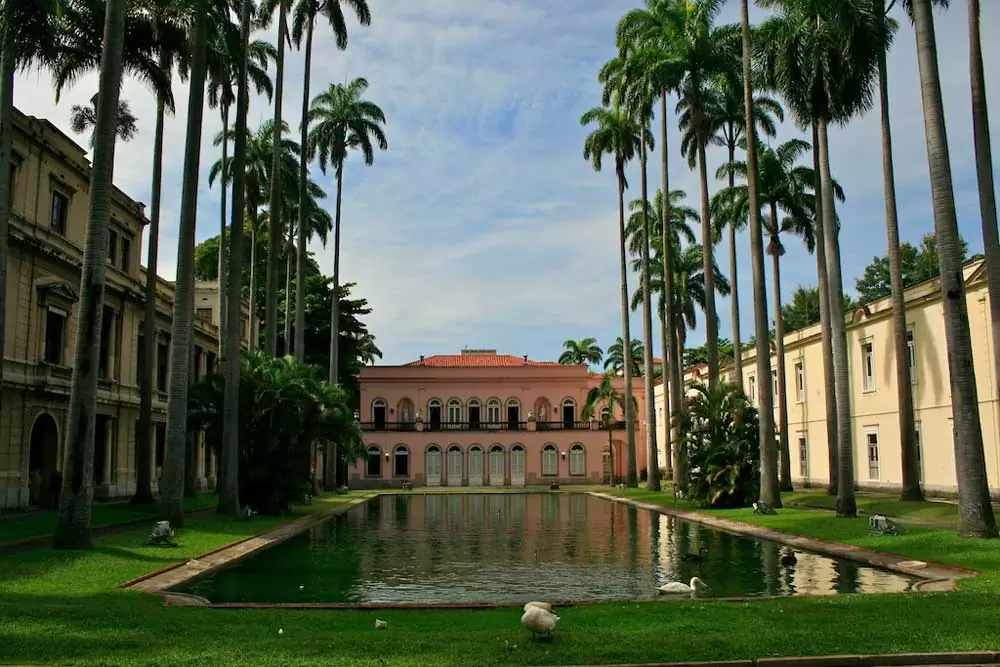 Palácio rosa, em frente a jardim com palmeiras imperiais e lago com patos, durante o dia em Museu Histórico e Diplomático do Itamaraty, no Centro do Rio de Janeiro