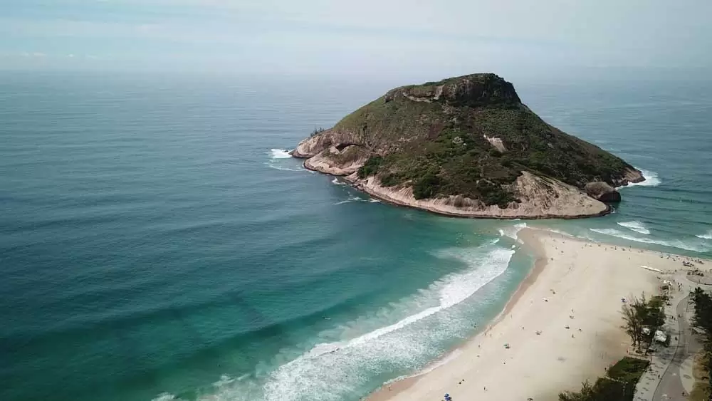 Vista área de mar e Pedra do Pontal, uma formação rochosa de com altitude de 125 metros, às margens da areia da praia do Recreio, no Rio de Janeiro