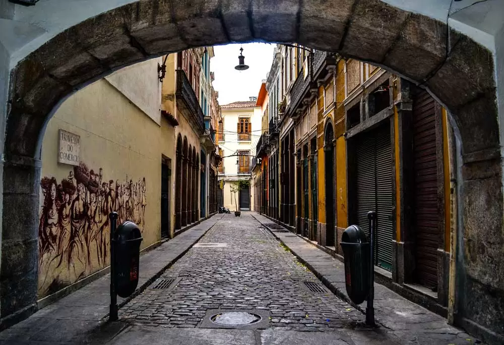 Arco colonial em rua de paralelepidedos, rodeada de construções coloridas, durante o dia, no Rio de Janeiro