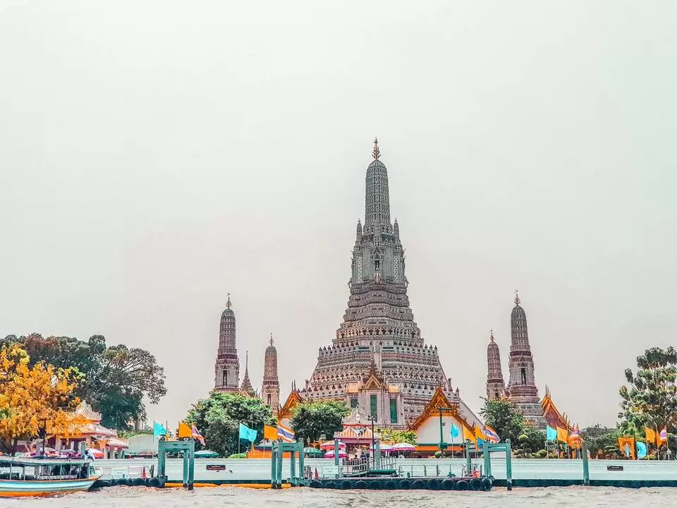 Construção branca e cinza, sob o céu nublado, conhecida como Wat Arun o Templo do Amanhecer, em Bangkok
