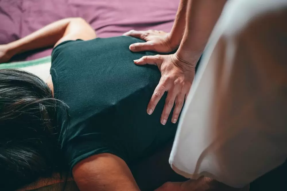 Mulher com blusa preta, deitada de costas, recebe massagem tailandesa