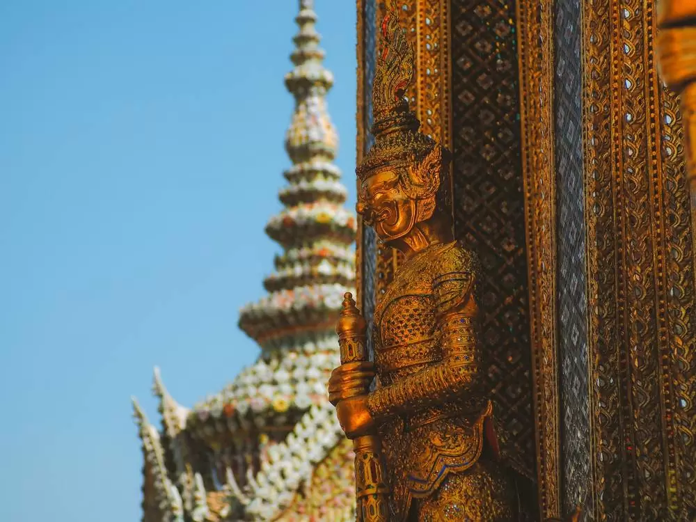 Estátua de homem dourada em frente a templo, durante o dia, em Bangkok, a capital da Tailândia