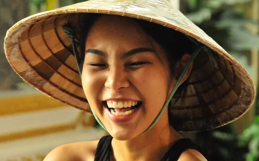 Mulher tailandesa com chapéu, sorri de olhos fechados