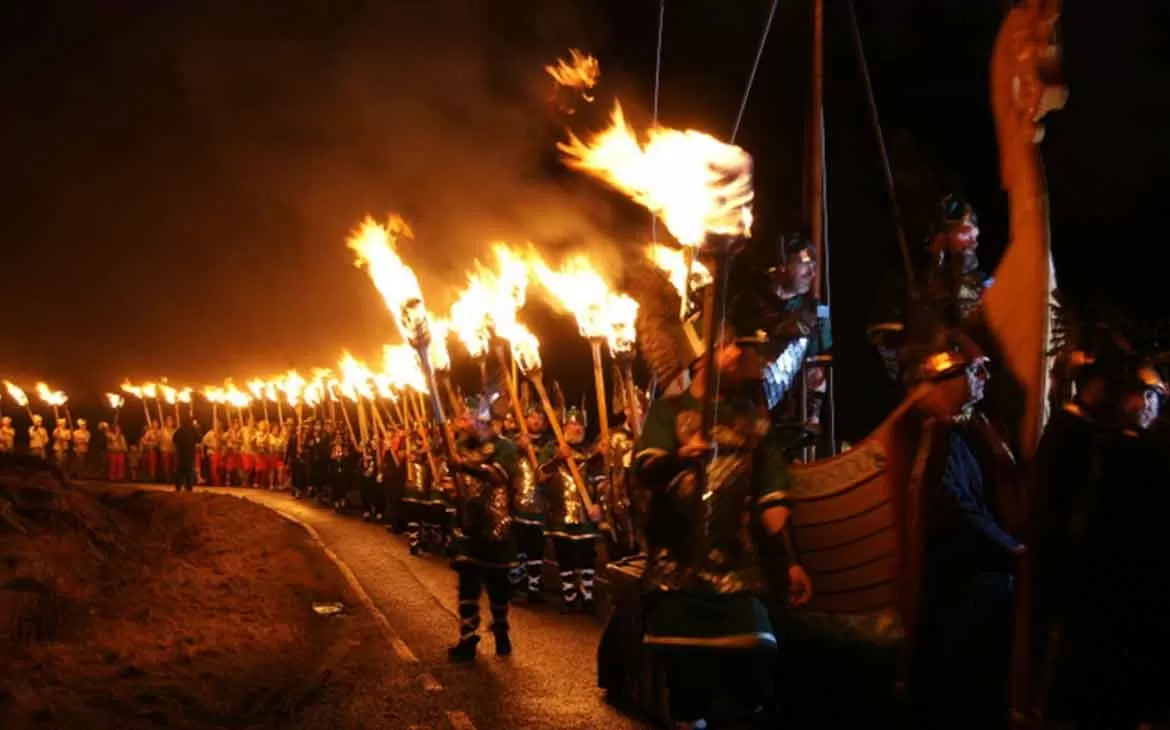Homens vestidos como vikings, segurando tochas de fogo, caminham em procissão do festival Up Helly Aa