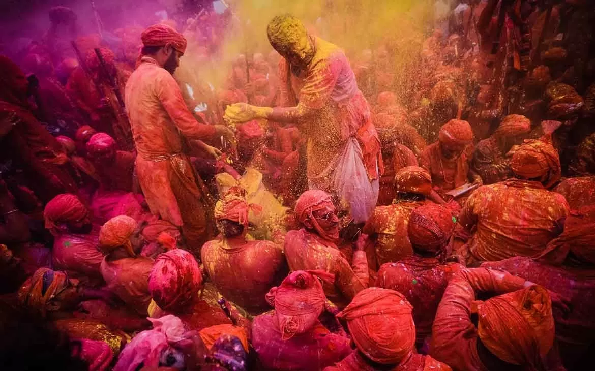 Pessoas com roupas sujas de pó rosa, jogam pó amarelo uma nas outras em Holi um festival que acontece na India