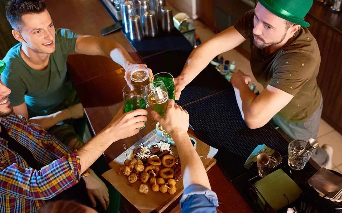 Homens vestidos de verde segurando copo com cerveja brindam em mesa de bar o Saint Patrick ‘s Day, data comemorada na Irlanda