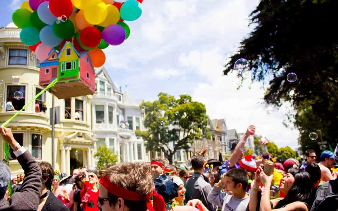 Pessoas vestidas com roupas coloridas conversam, riem, sopram bolinhas de sabão e carregam balões coloridos durante Bay to Breakers uma ocorrida anual que acontece em São Francisco