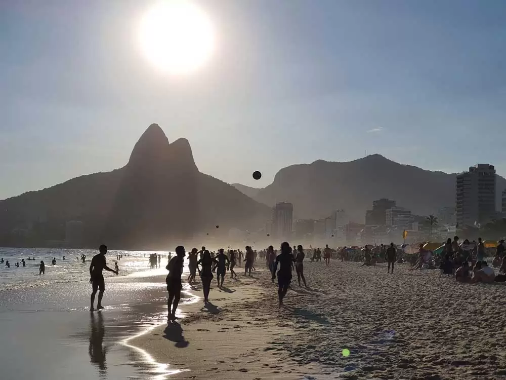 Silhueta de pessoas jogando bola em areia de praia no Rio de Janeiro, durante o dia