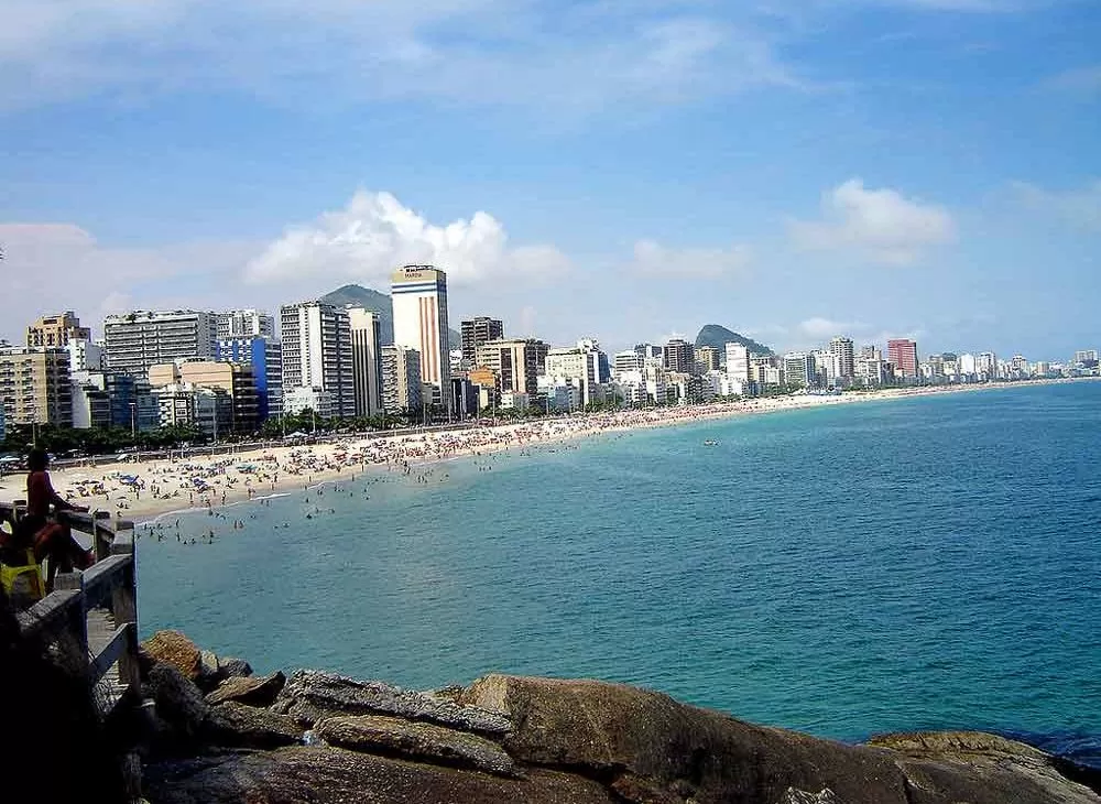 Pessoas em mirante observam mar, areia e construções ao redor de praia do Leblon, no Rio de Janeir