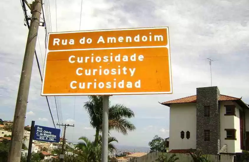 Em um dia nublado, placa com frase 'rua do amendoim - curiosidade, curiosity e curiosidad -, localizada em rua de São Thomé das Letras