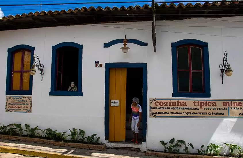 cozinheira, parada em porta de restaurante, olha para rua em São Thomé das Letras