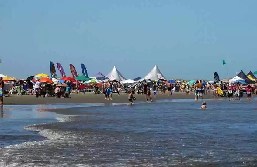 Em um dia ensolarado, paisagem da praia com pessoas, tendas e guarda-sóis