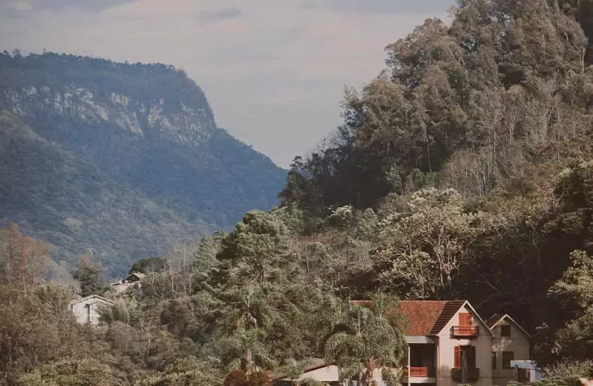 casas em frente a montanhas cobertas por árvores, durante o dia em caxias do sul, um dos lugares para viajar no Rio Grande do Sul