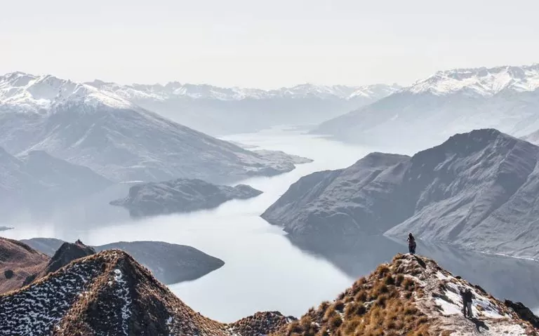 viajantes tiram fotos em cima de montanha com vista para o mar na nova Zelândia, durante o dia