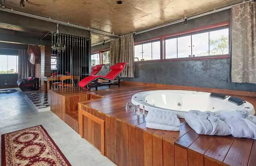 cadeira vermelha e banheira de hidromassagem em suíte ampla de pousada loft da serra