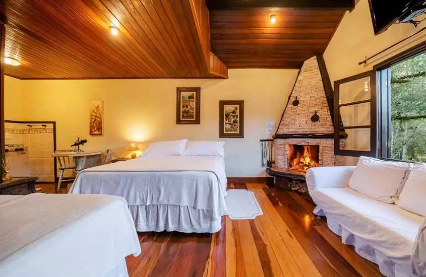 cama de casal, sofá e lareira em suíte de pousada cantos e contos, um dos destinos românticos em Minas Gerais