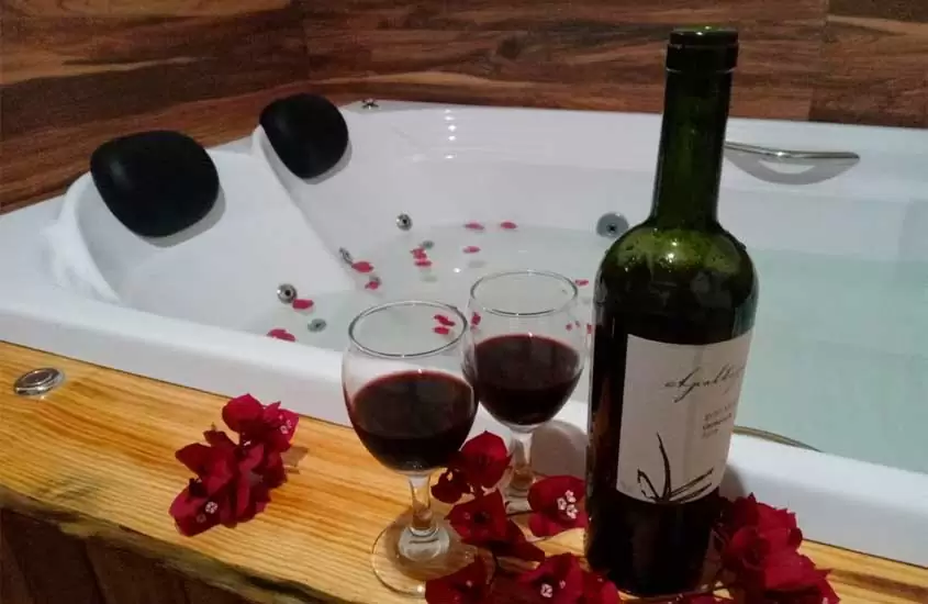 Área de banheira com taças de vinho, flores e deck de madeira