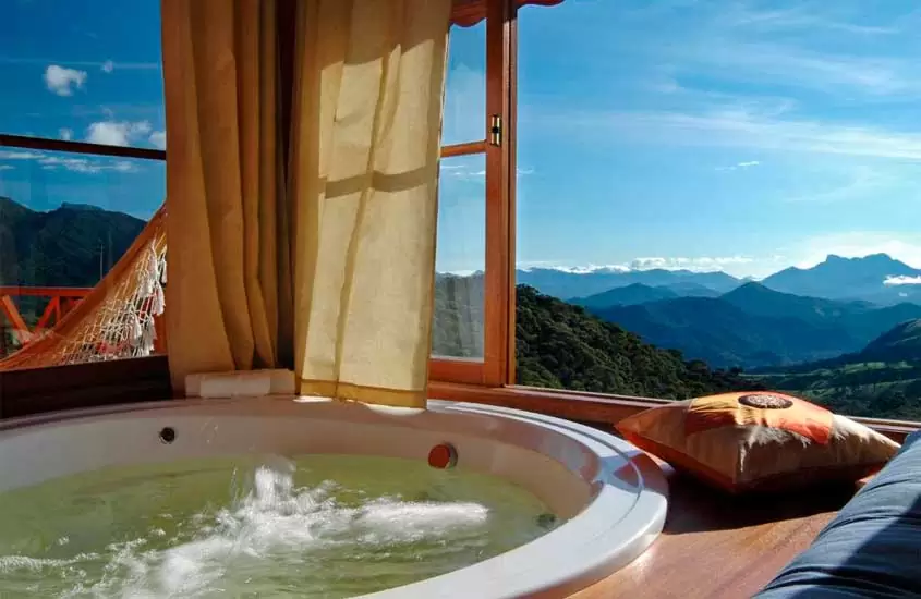 Área de banheira de pousada em visconde de maua com janelas grandes, rede de descanso na varanda e paisagem das montanhas