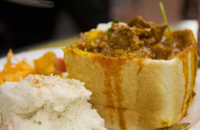 prato branco com pão vazado, recheado com curry picante, uma comida da África do sul