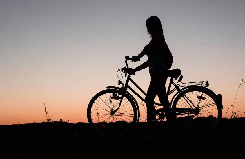 silhueta de mulher com bicicleta admirando o pôr do sol