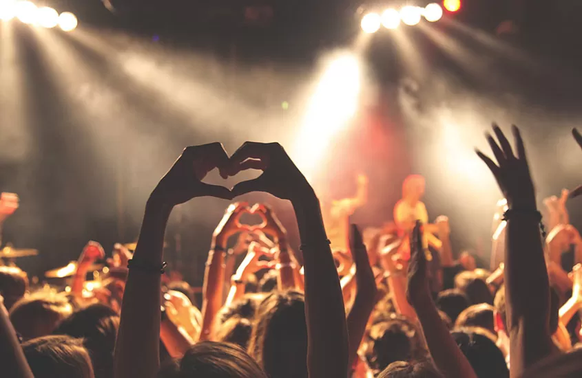 pessoas fazem coração com as mãos em direção ao placo, durante um show em morro de Sao Paulo