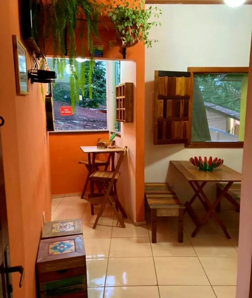 plantas, mesas e cadeiras de madeira em sala de Bicho Preguiça Hostel, uma opção para quem busca onde ficar em Trindade