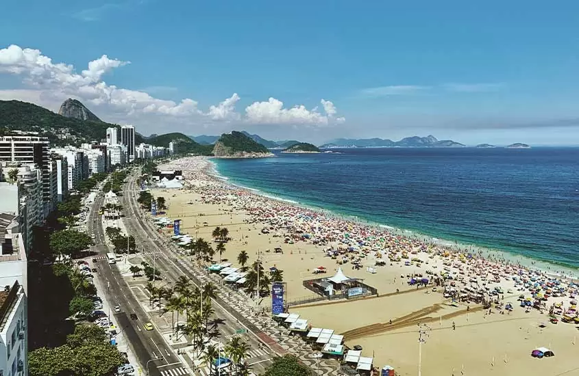 vista aérea de carros em avenida, pessoas em areia e mar durante o dia em Copacabana, uma opção de onde ficar no rio de janeiro