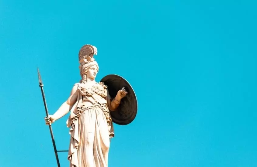 estatua de mármore sob céu azul segurando lança e escudo