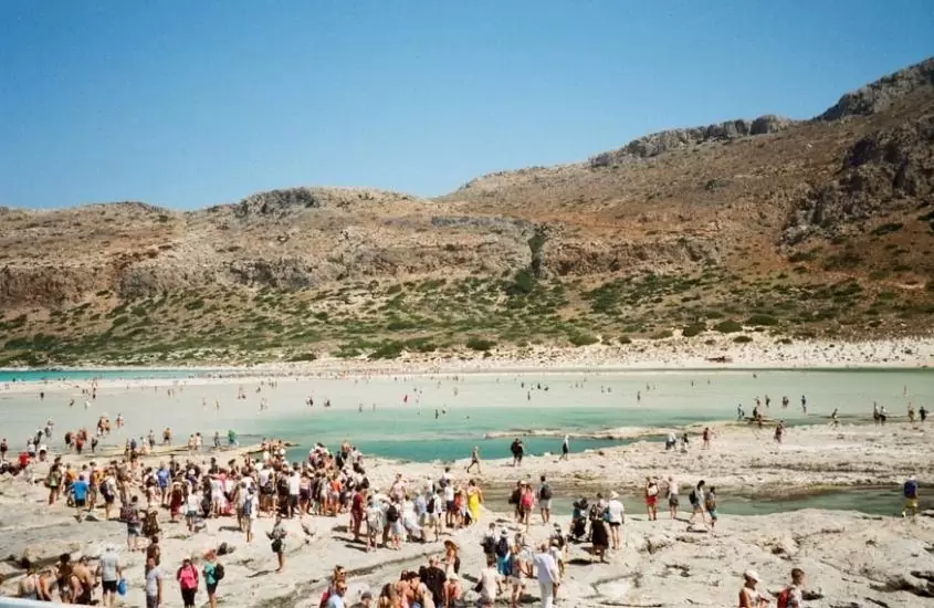 pessoas em areia e mar de uma das praias da grécia durante dia ensolarado