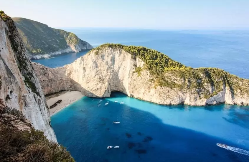 barcos em água azul cristalina perto de formações rochosas, durante o dia em uma das ilhas gregas