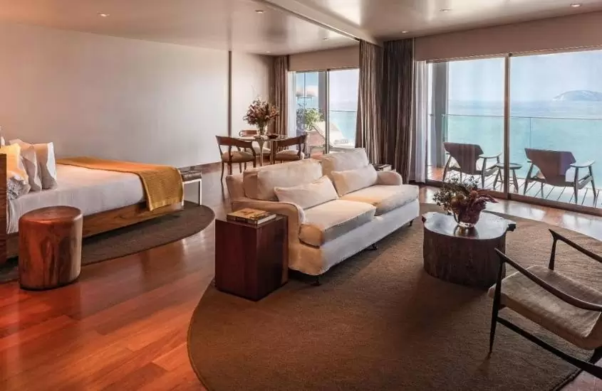 suíte de hotel fasano onde há quarto com cama, sofá, mesa e cadeiras e varanda com cadeiras com vista para o mar