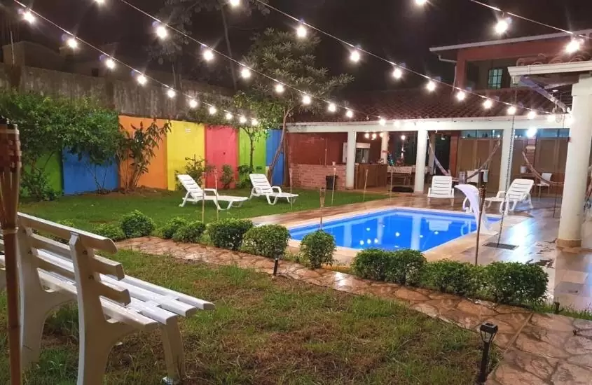 espreguiçadeiras brancas em frente a piscina em quintal com plantas de teko arte hostel & bar, hospedagem no paraguai