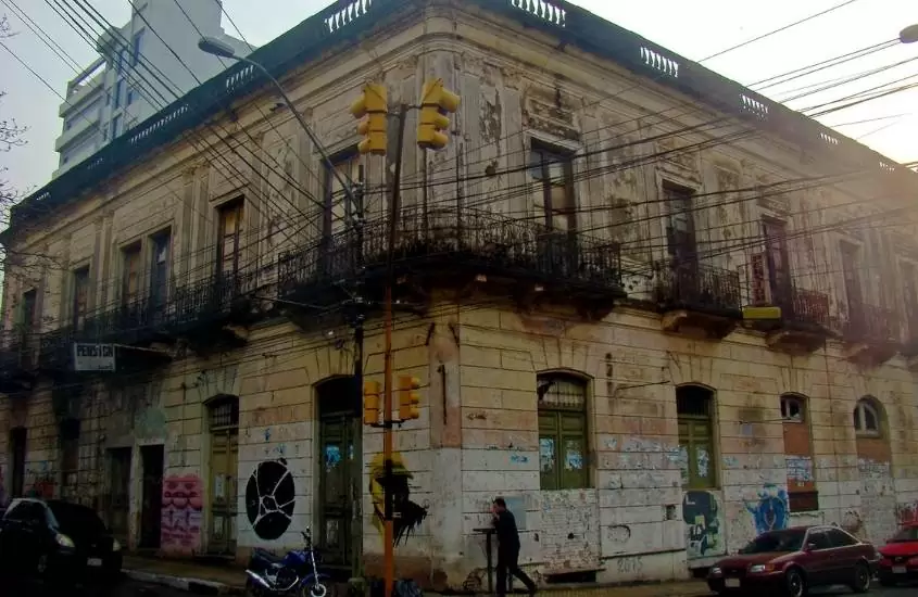 homem caminhando ao lado de construção antiga de dois andares em rua de paraguai