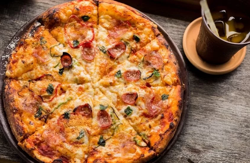 pizza e copo com bebida em cima de mesa de madeira