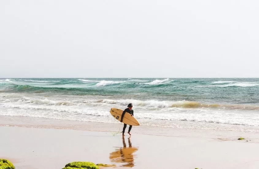 homem caminhando em frente ao mar durante o dia segura prancha de surf