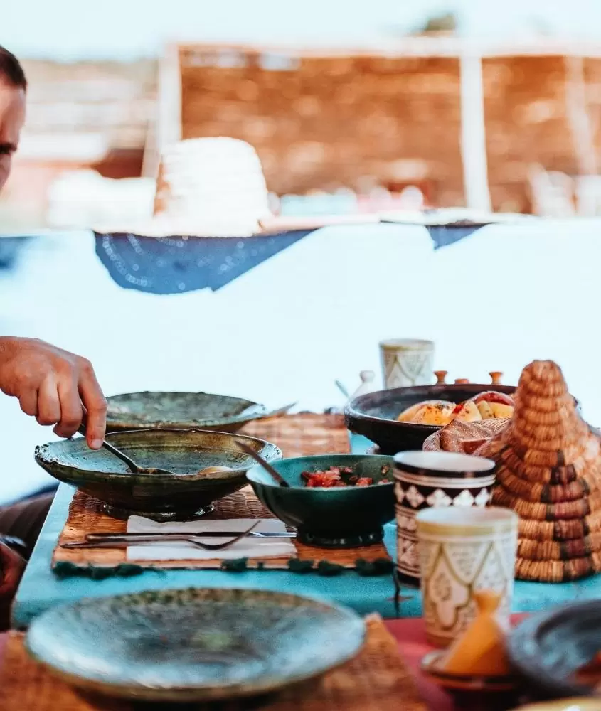 homem coloca comida dentro de prato que está em mesa cheia de comidas típicas do marrocos