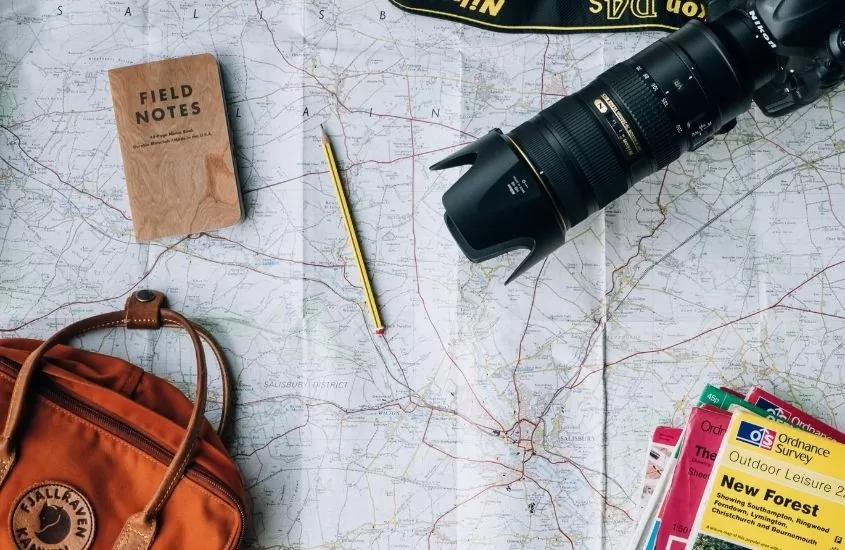 caderno, mochila, revistas, câmera e lápis em cima de mapa de papel