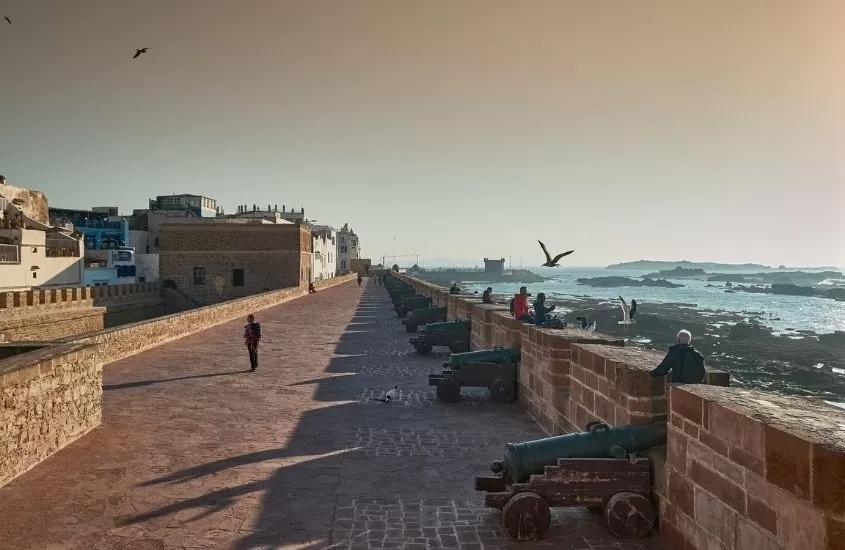 pessoas sentadas em rente ao mar observam pôr do sol em essaouira, uma ótima atração para quem busca o que fazer no marrocos