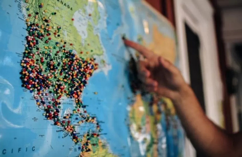 pessoa aponta mão para mapa mundial marcado com pins