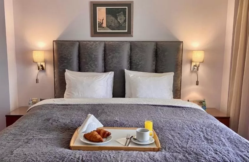 café, suco e croissant em bandeja em cima de cama de casal de quarto do art 'otel, um hotel na capital da bulgária