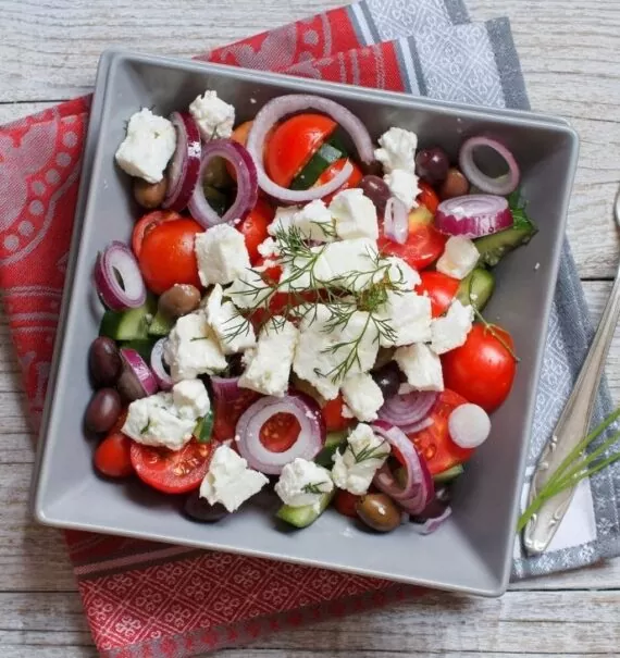 salada grega, uma das comidas gregas, dentro de prato cinza quadrado