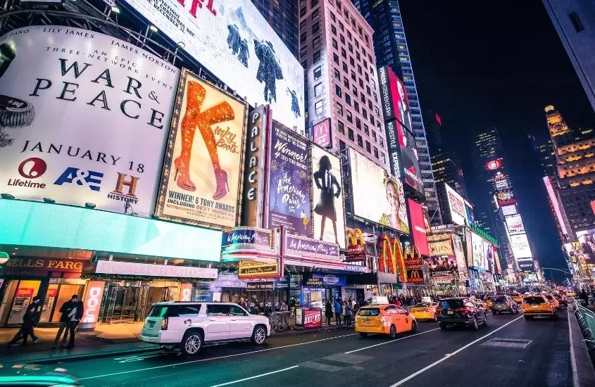carros passam em times square, avenida com prédios iluminados em nova york, um dos lugares mais caros do mundo para viajar