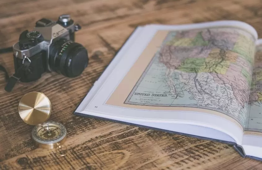 livro com mapa, câmera e bússola em cima da mesa de madeira