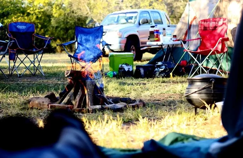 fogueira e cadeiras em gramado de camping, durante o diav